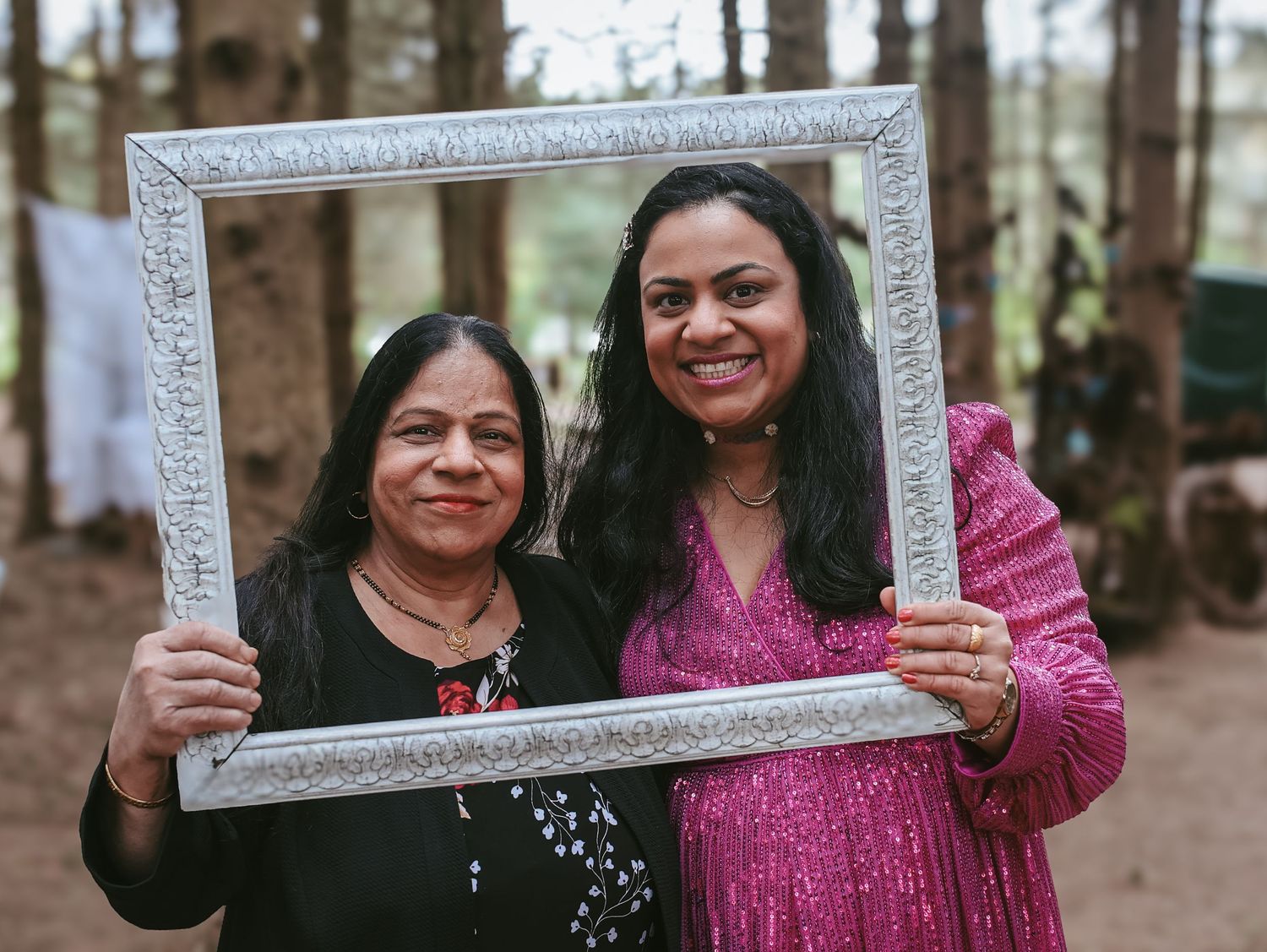 Three friends pose with a decorative silver frame in an outdoor wooded setting.