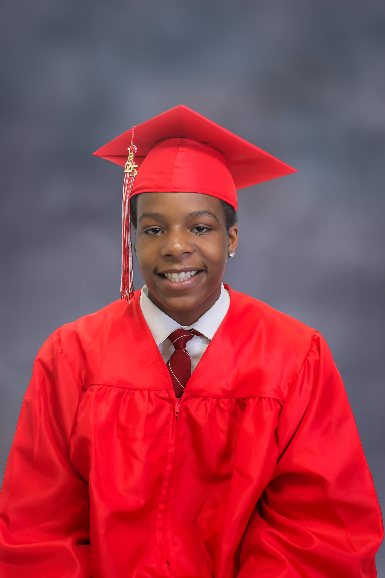 Graduate wearing bright red cap and gown with matching tie smiles warmly in formal portrait against gray backdrop.