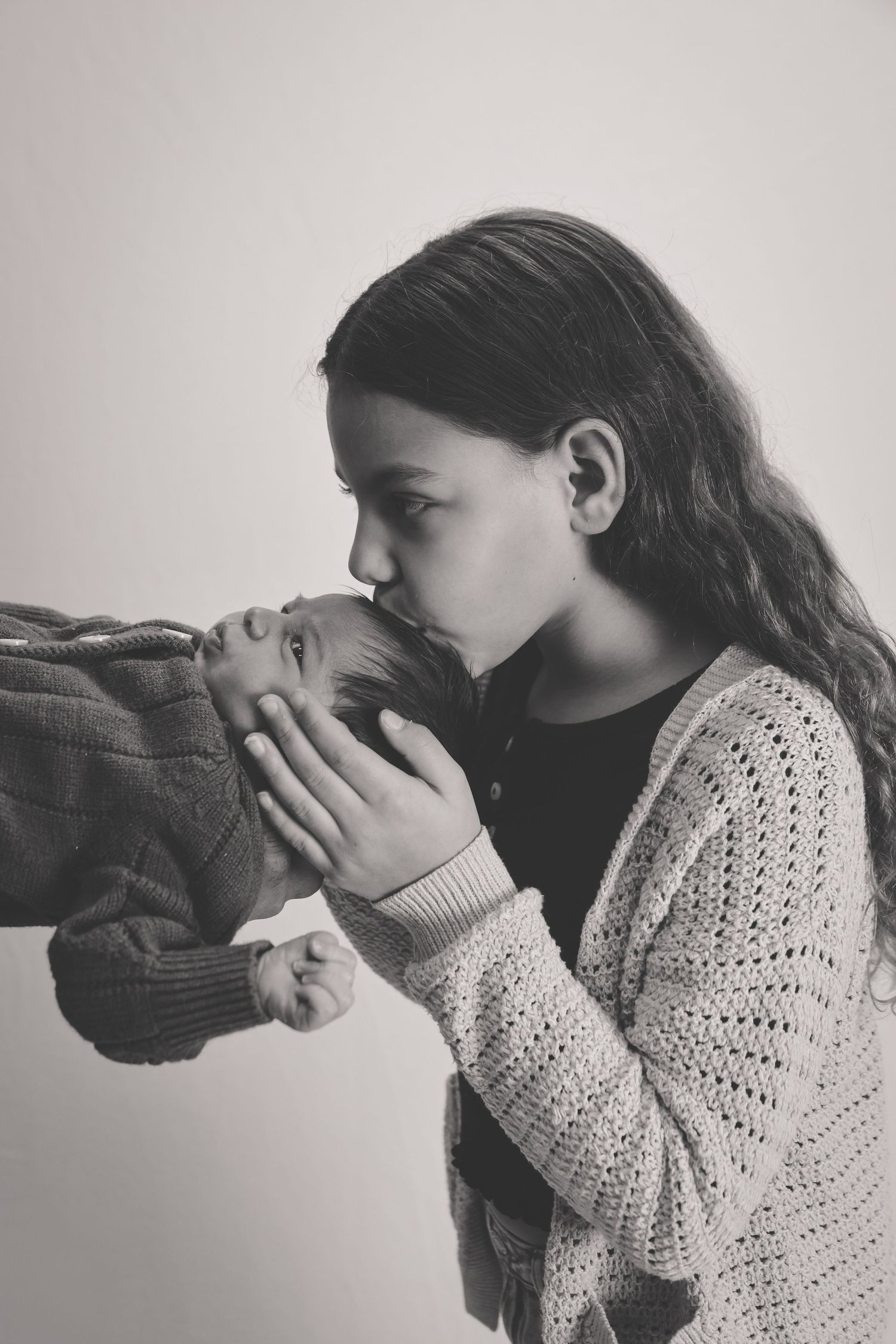 A child in a knit sweater kisses a parent's hand in a tender black and white portrait.