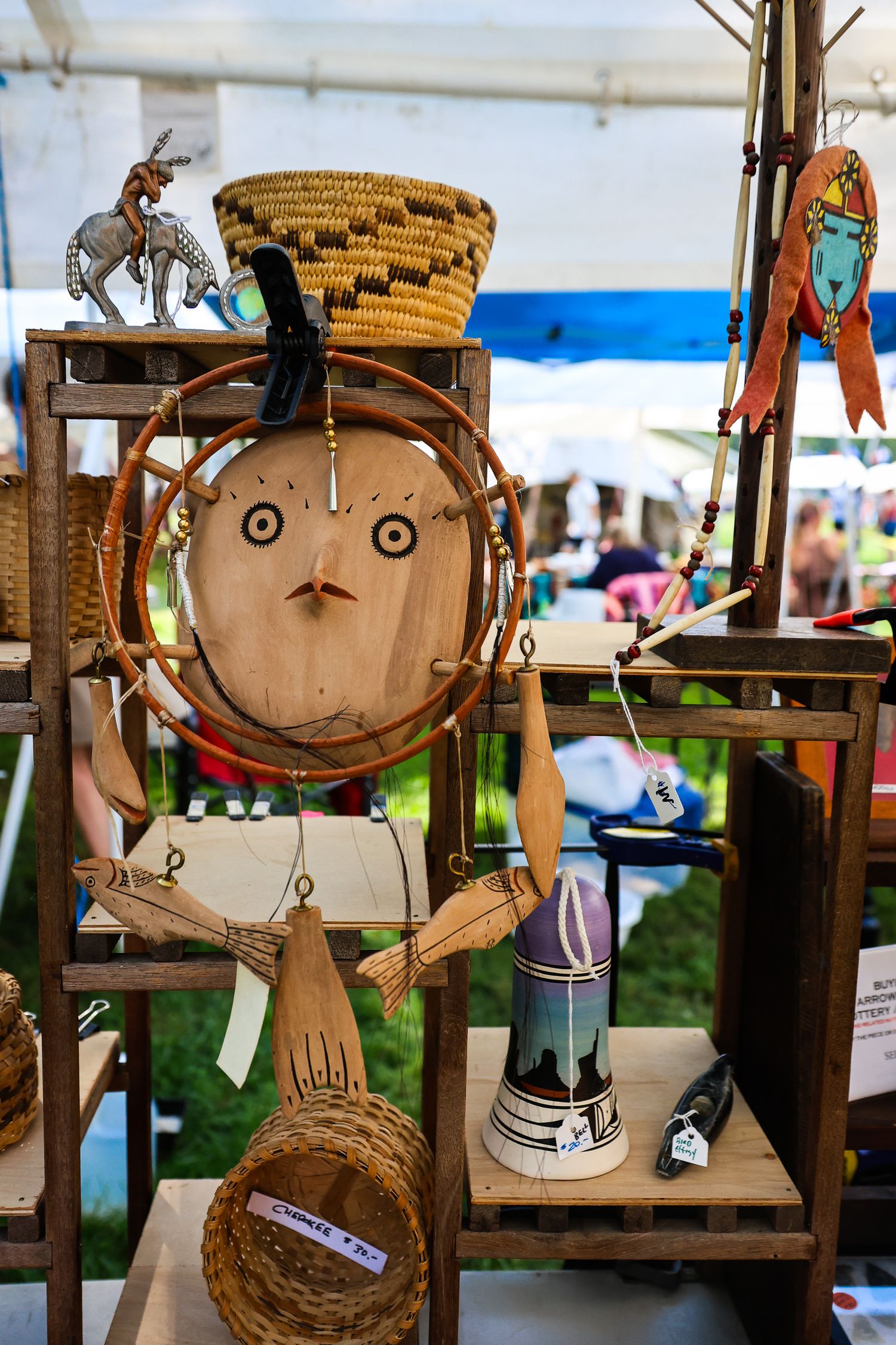 Handmade wooden folk art faces with simple features displayed at an outdoor craft market.