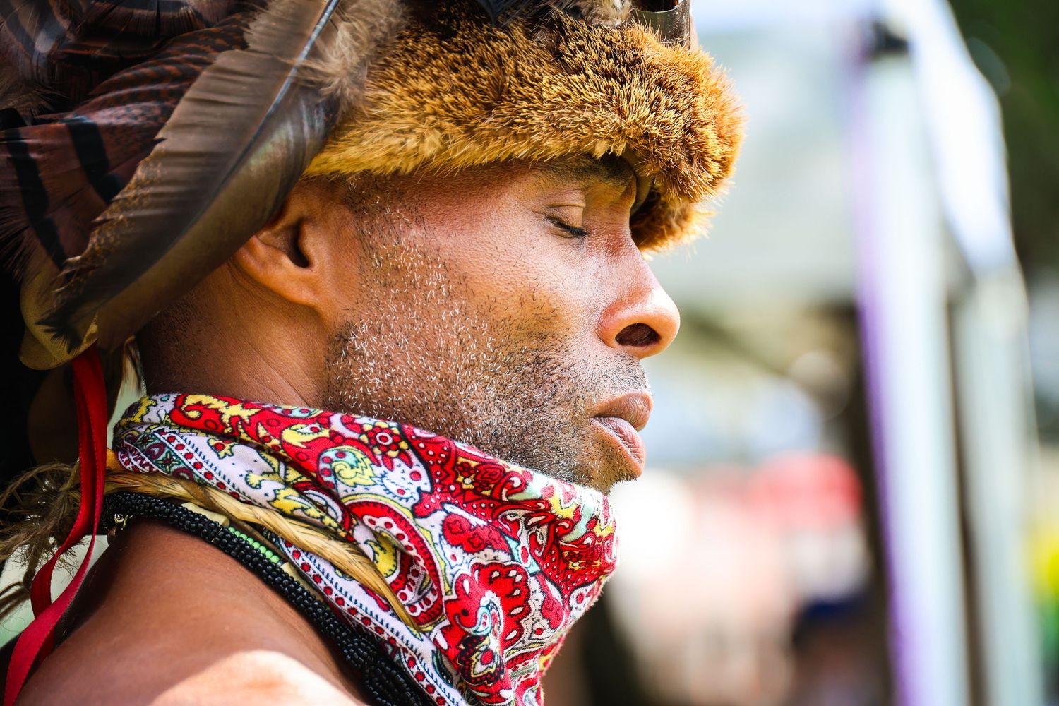 A person wearing a red bandana face covering stands in profile against a blurred background.