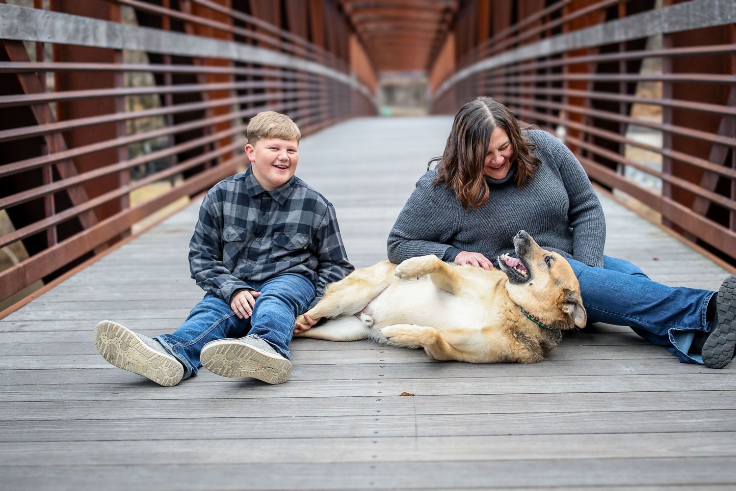 Family and their golden retriever dog sitting together on a wooden bridge for outdoor portraits.