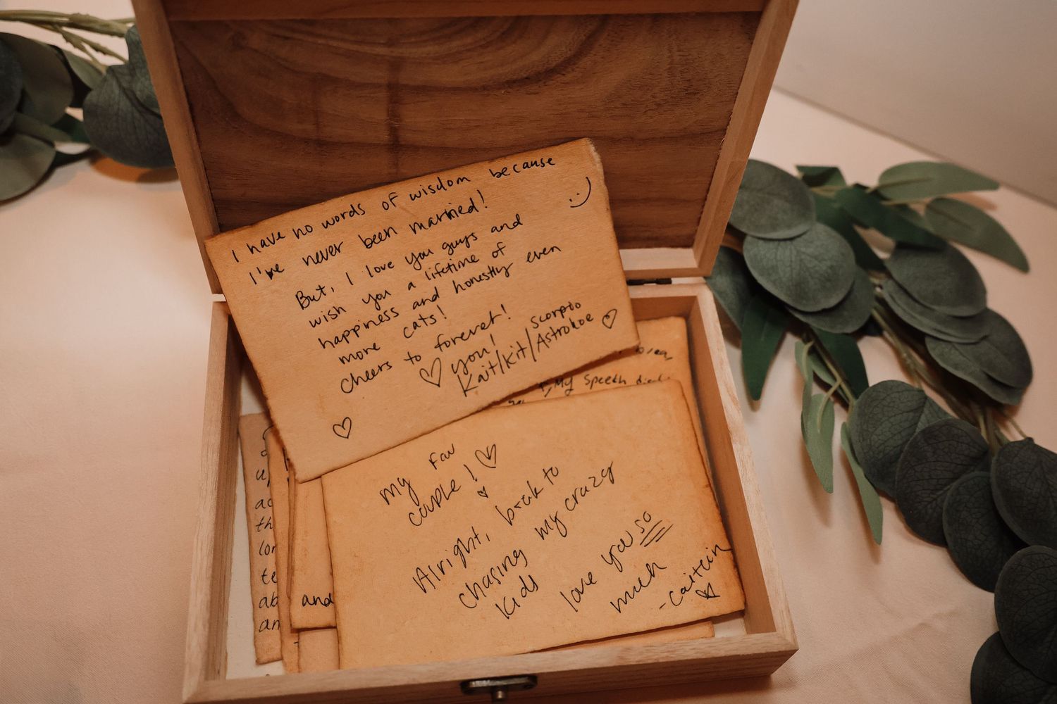 Handwritten recipe cards and green leaves arranged on a wooden surface in warm lighting.
