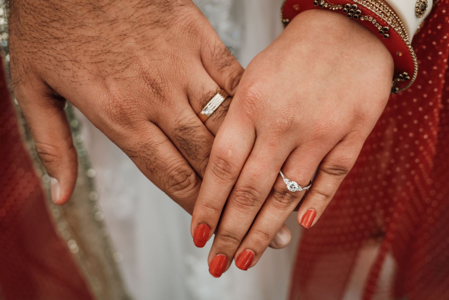 Close-up of hands wearing wedding rings with red painted nails and traditional Indian bracelets.