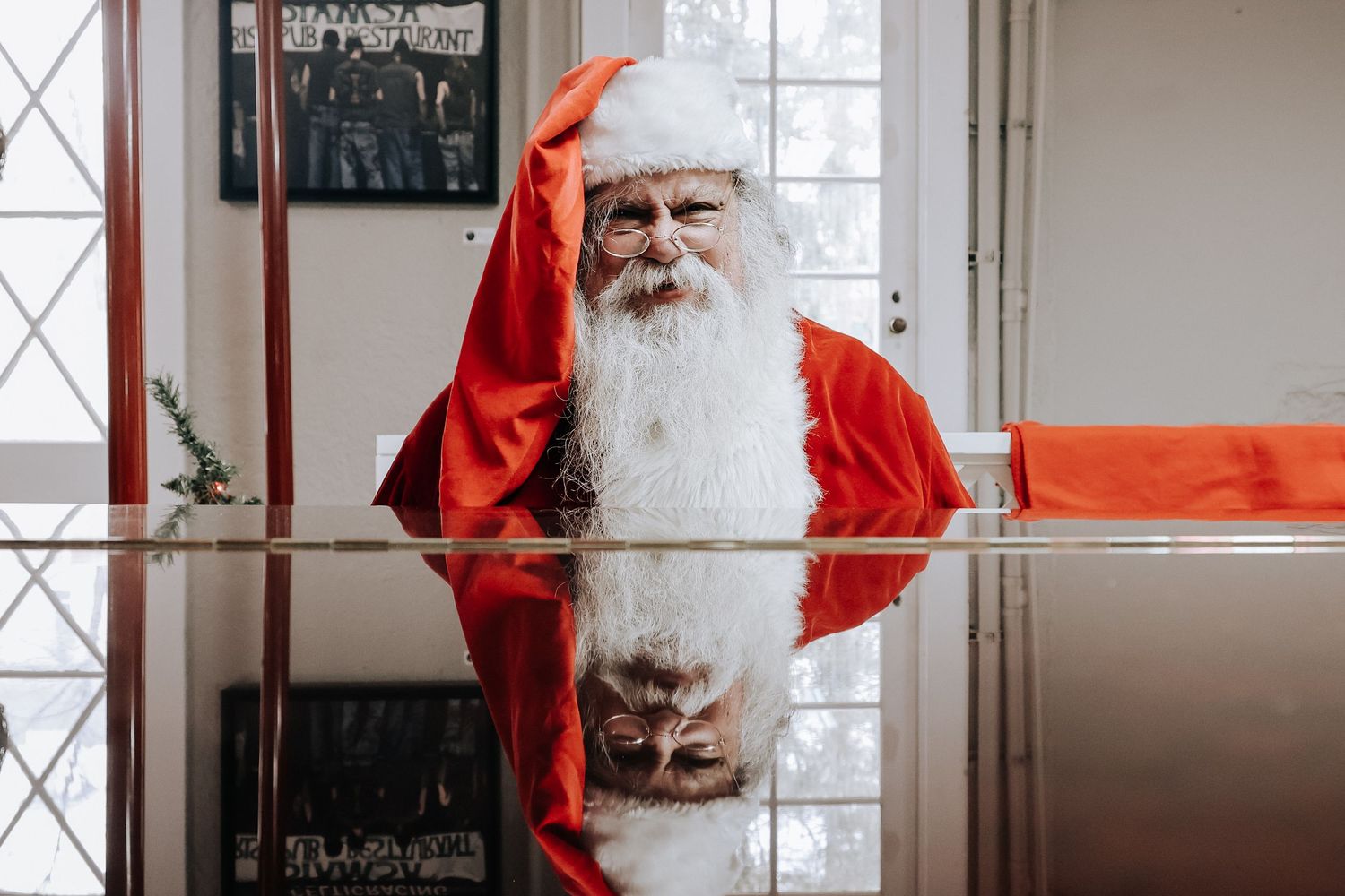A figure in a red Santa Claus suit sits in a bright white room with window panes visible in the background.