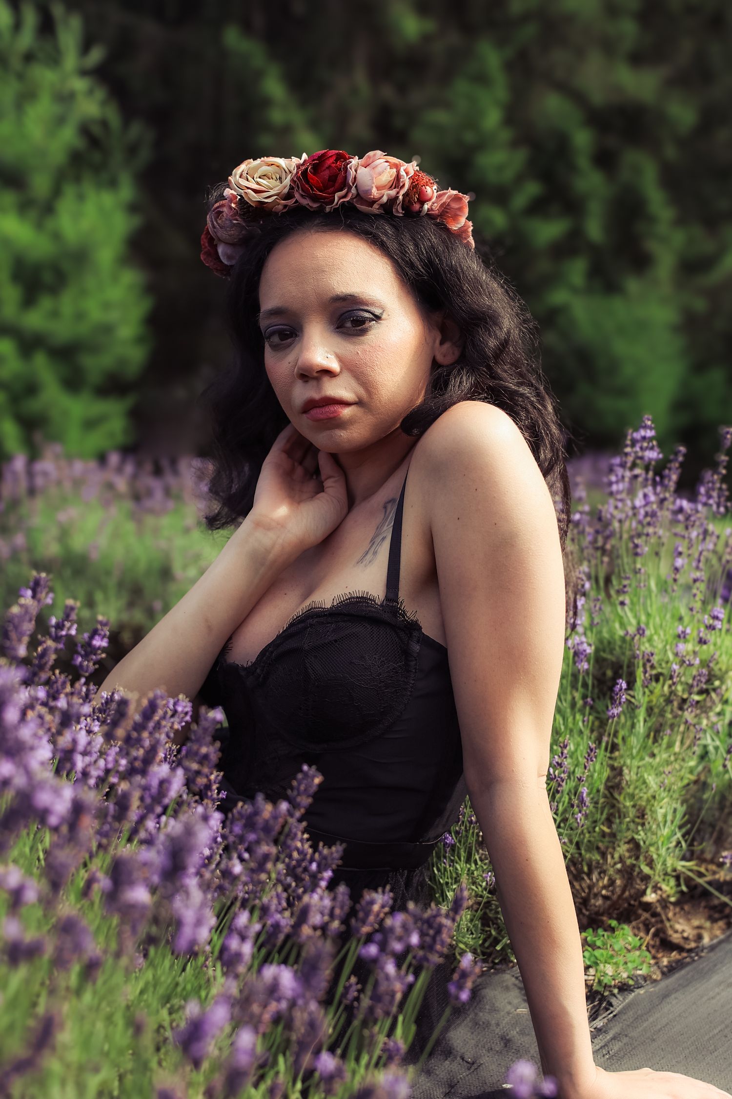 A woman in a black dress poses in a garden with blooming purple lavender flowers and floral hair accessories.