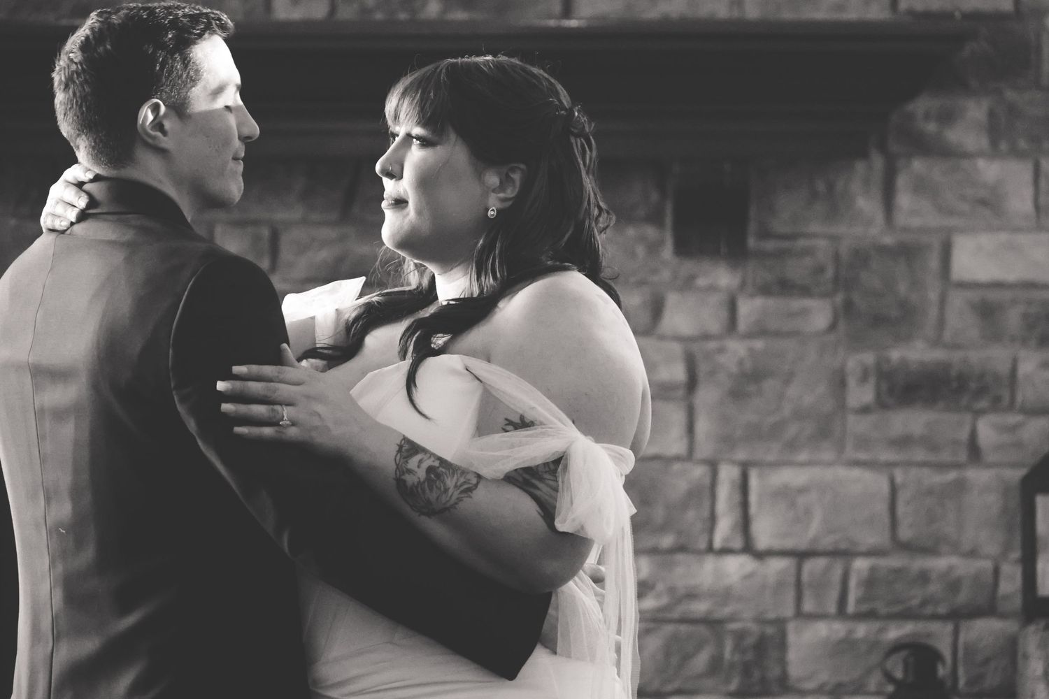 A black and white romantic moment between a couple at their wedding against a stone wall backdrop.