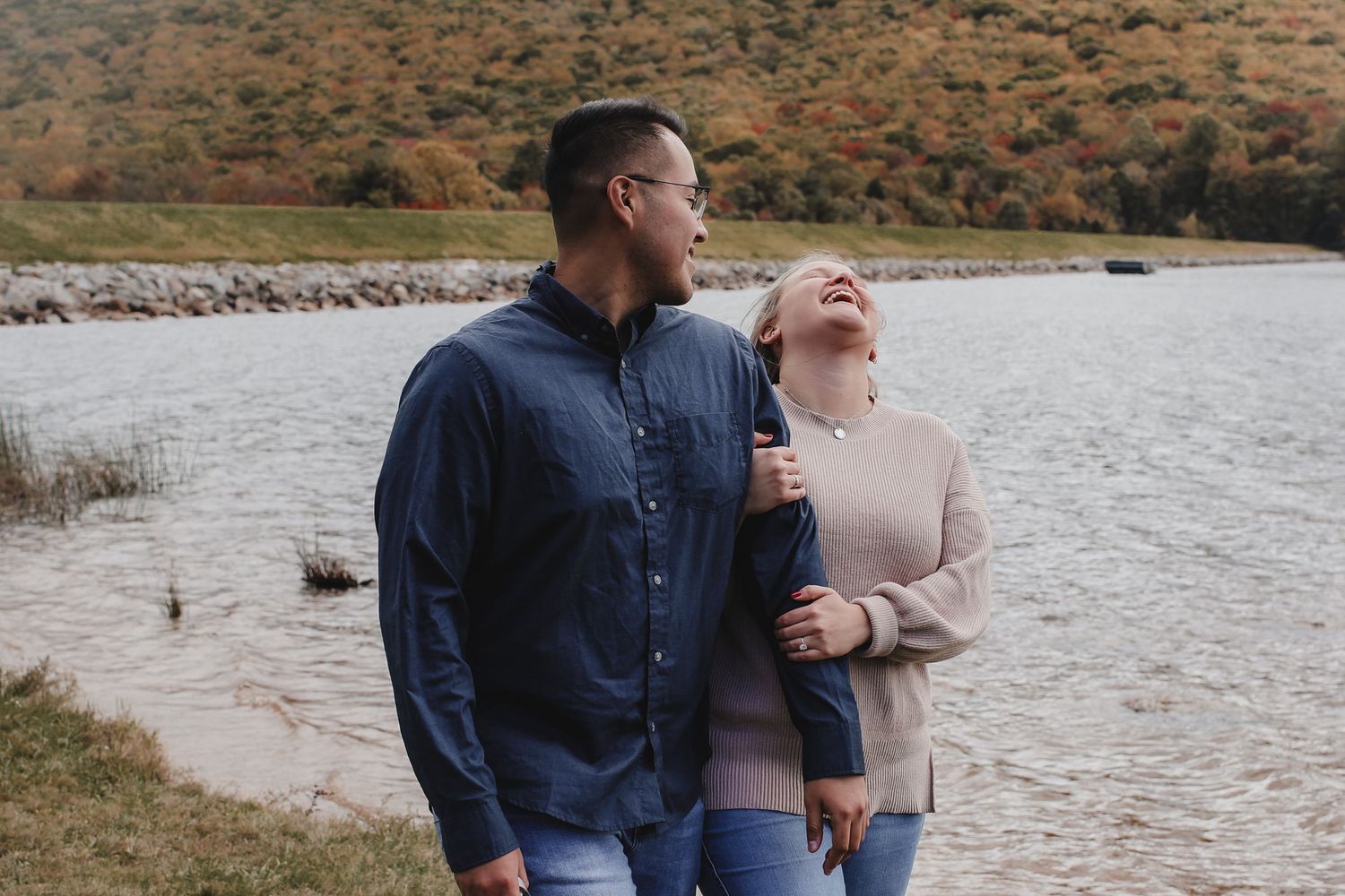 Couple enjoying a romantic moment together while walking along a scenic waterfront path on an autumn day.