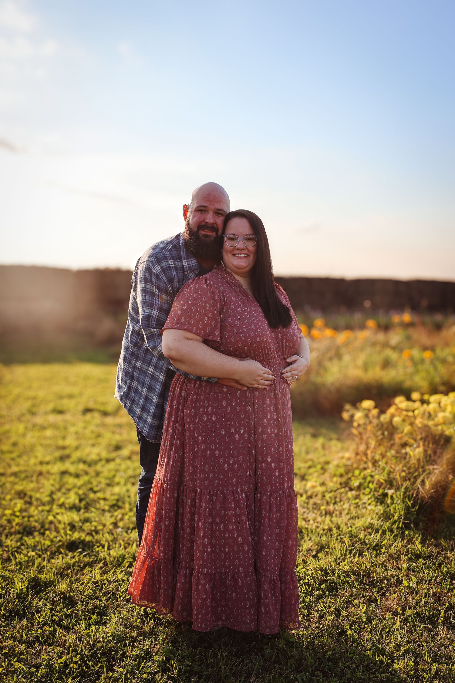 A couple embraces in a golden sunlit meadow during sunset with yellow wildflowers in the background.