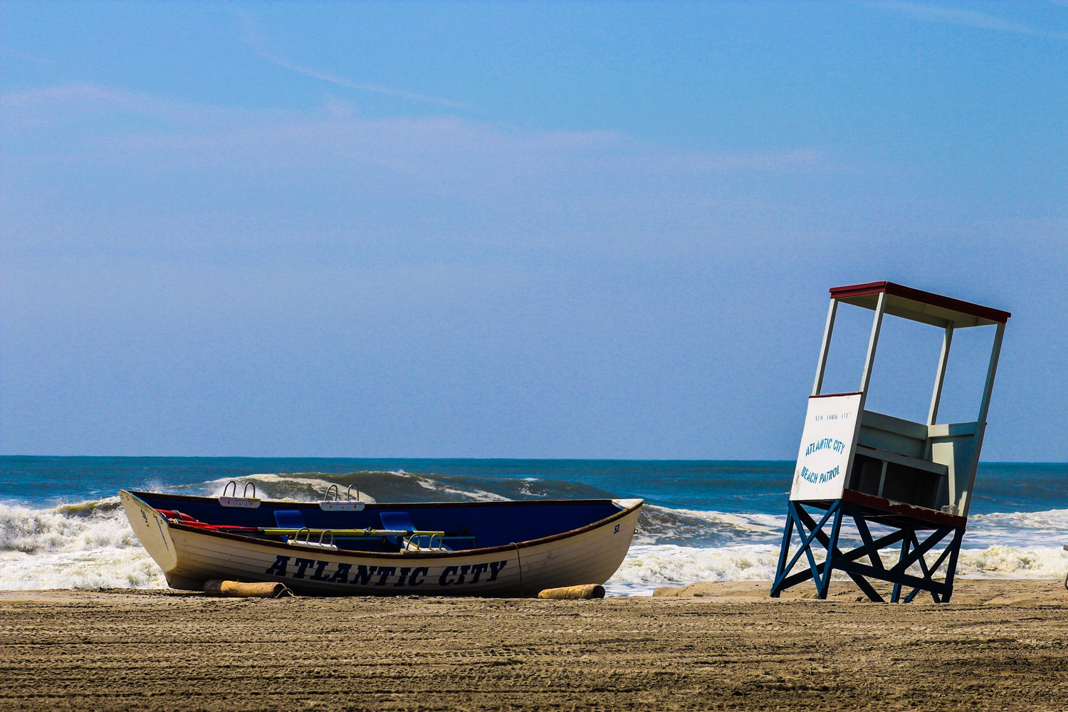 Atlantic City lifeguard stand and rescue boat on sandy beach with ocean waves and blue sky backdrop.