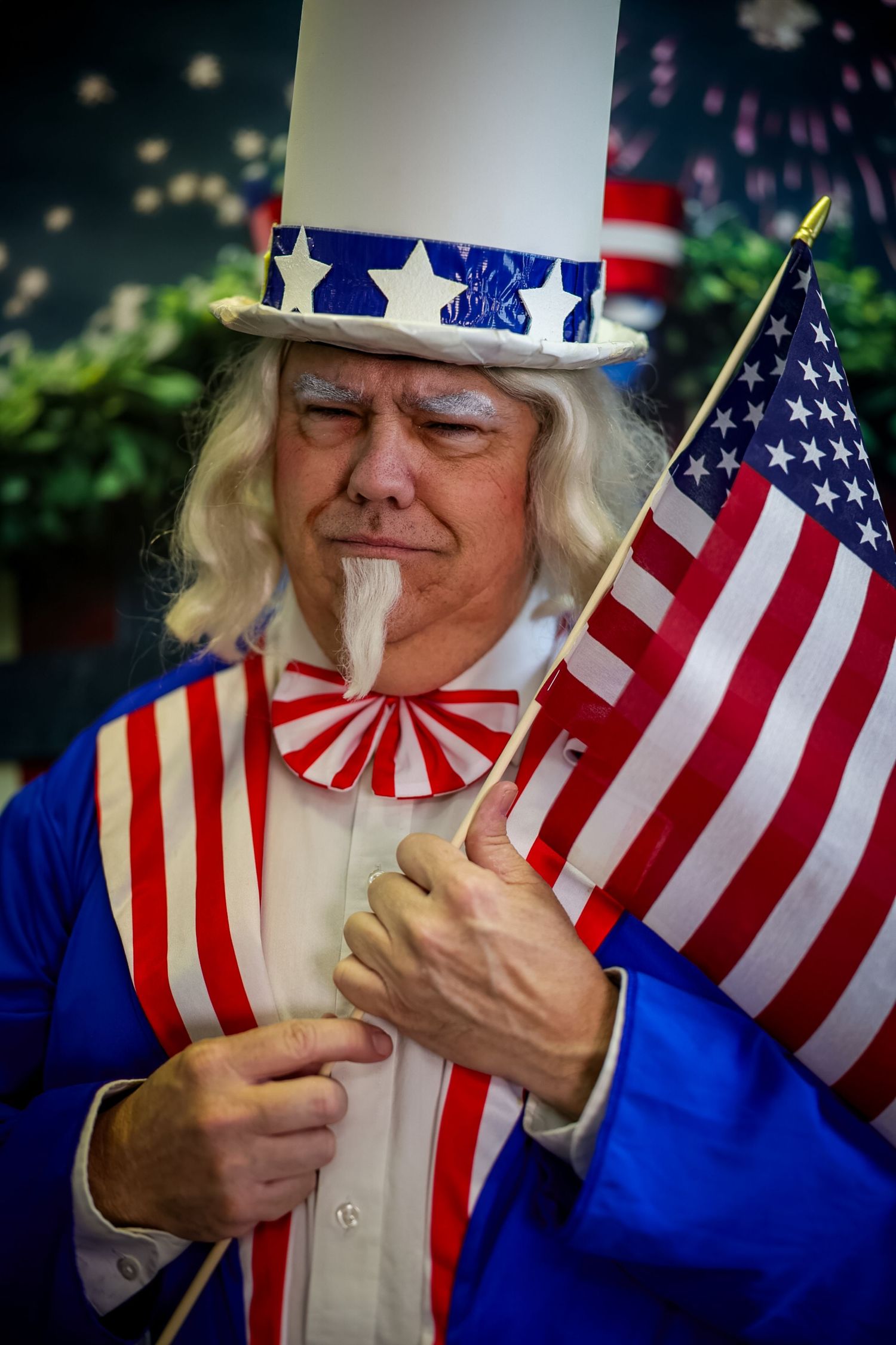Man dressed as Uncle Sam in patriotic costume holding American flag at Fourth of July celebration.