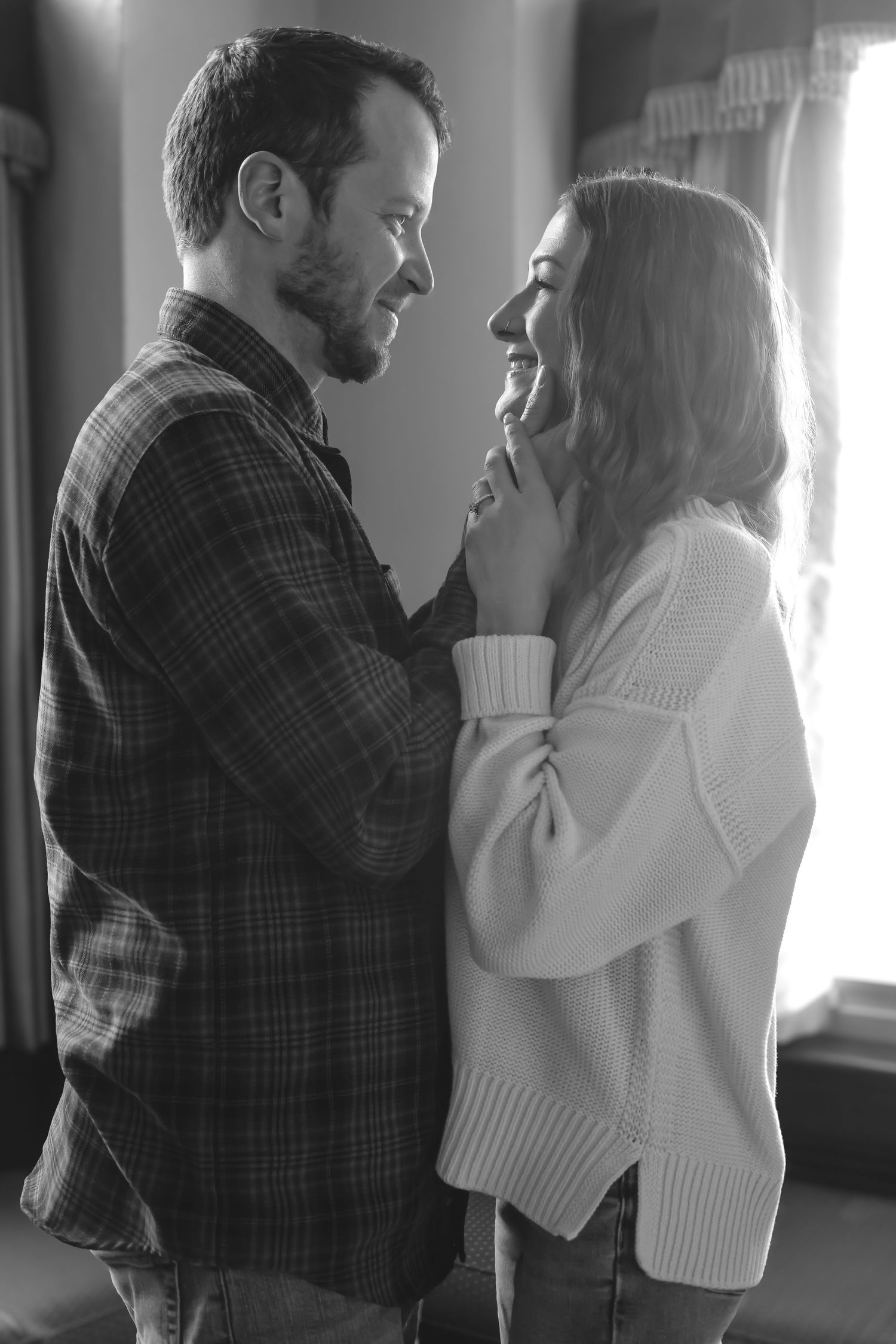 A romantic black and white portrait of a couple in casual sweaters sharing an intimate moment together.
