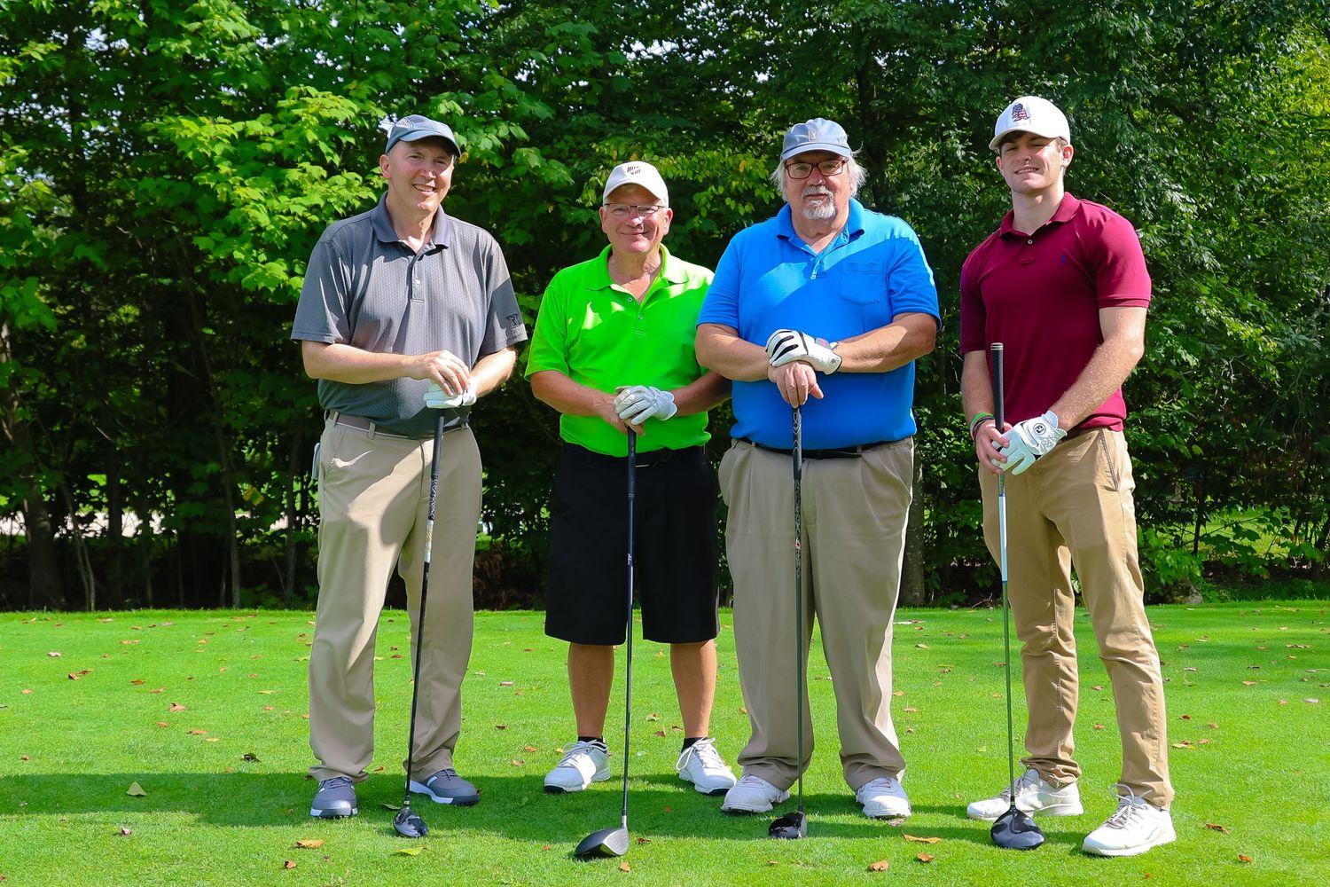 Golfers line up on a lush green course holding their clubs and wearing casual golf attire.