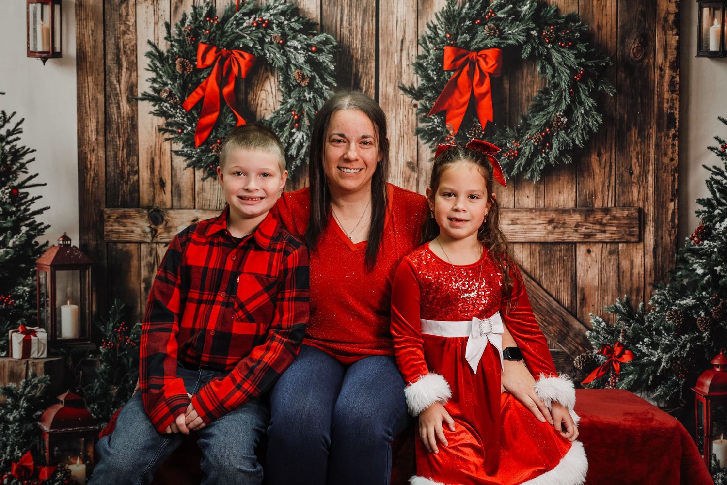 Family wearing coordinating red and black buffalo plaid outfits poses for holiday photos against rustic wooden backdrop.