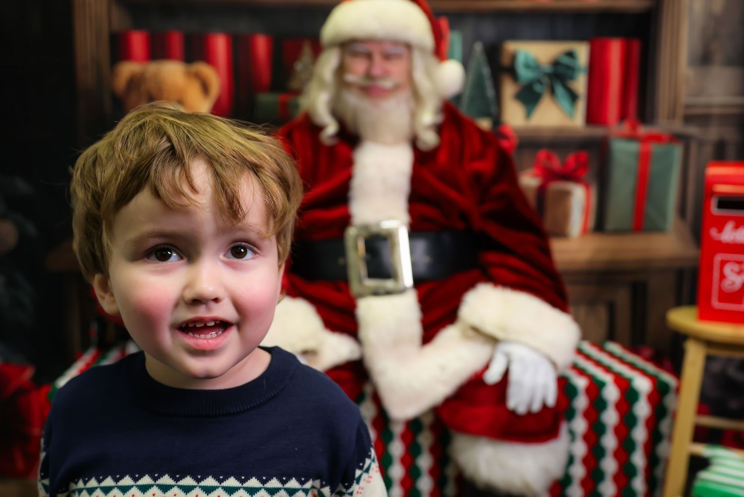 A child with a delighted expression visits Santa Claus at a festive holiday display with red decor and twinkling lights.
