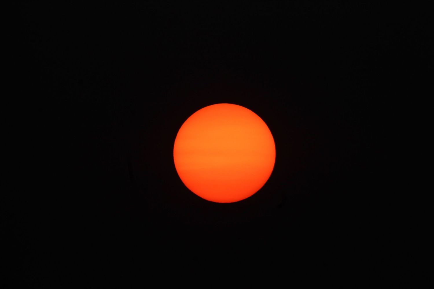 A bright orange sun glows against a dark sky during sunset or sunrise.
