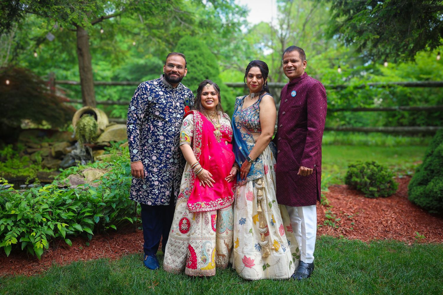 A group of people in colorful traditional outfits pose together in a lush garden setting.