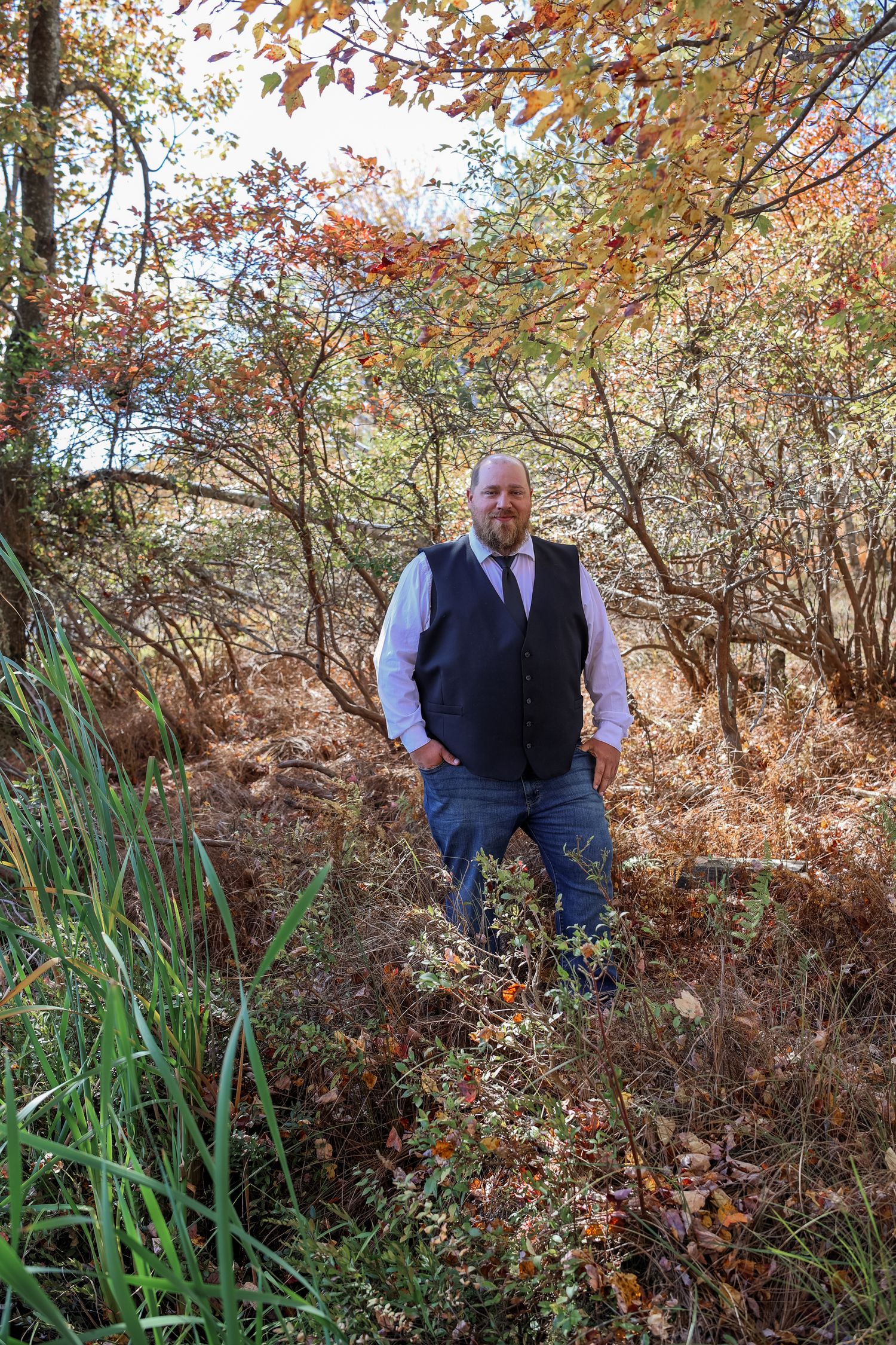 A person explores a wooded area with autumn foliage and tall grass during fall season.