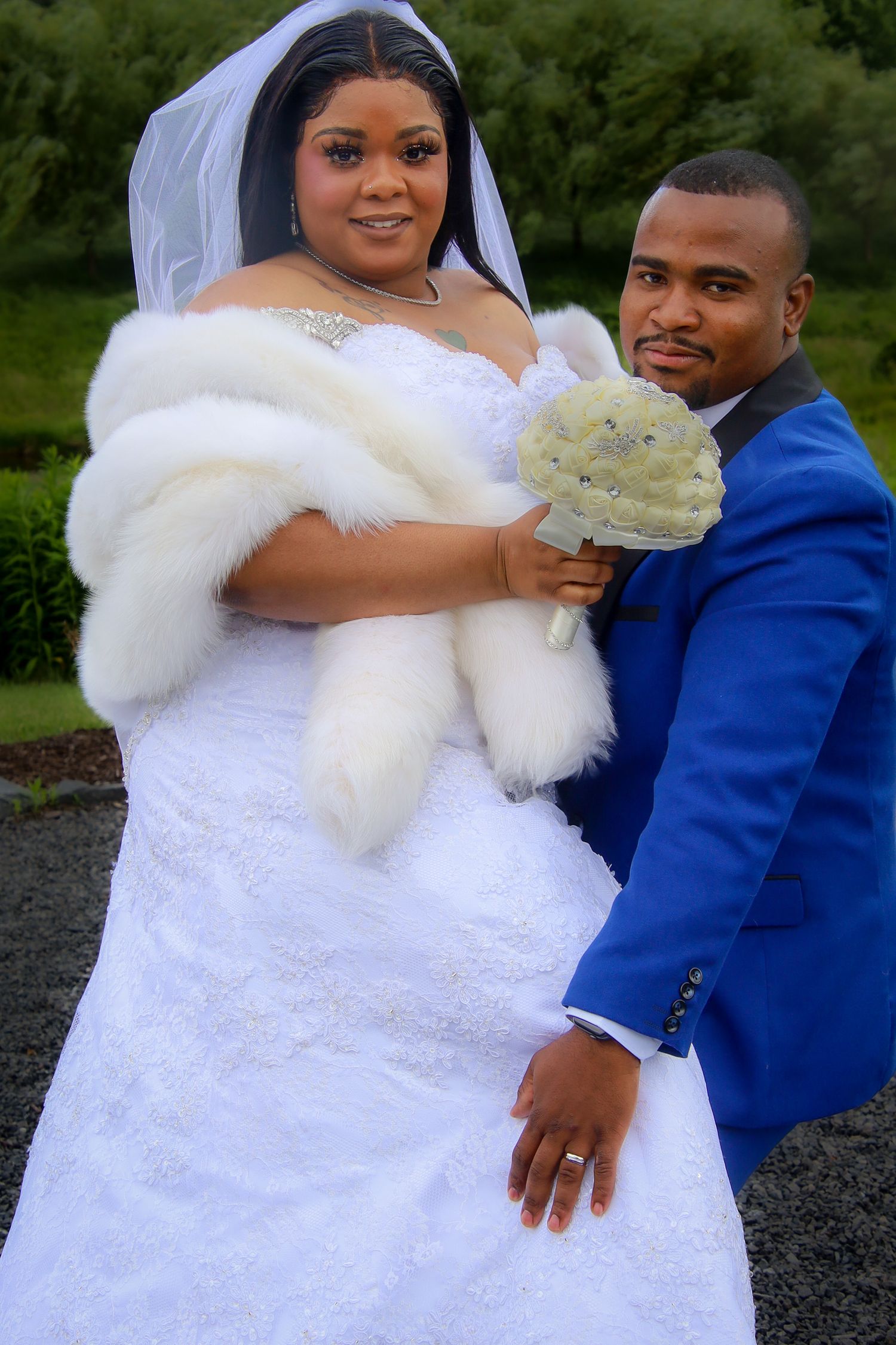 A bride in a white gown with fur trim and groom in a royal blue suit pose together during their wedding photoshoot.