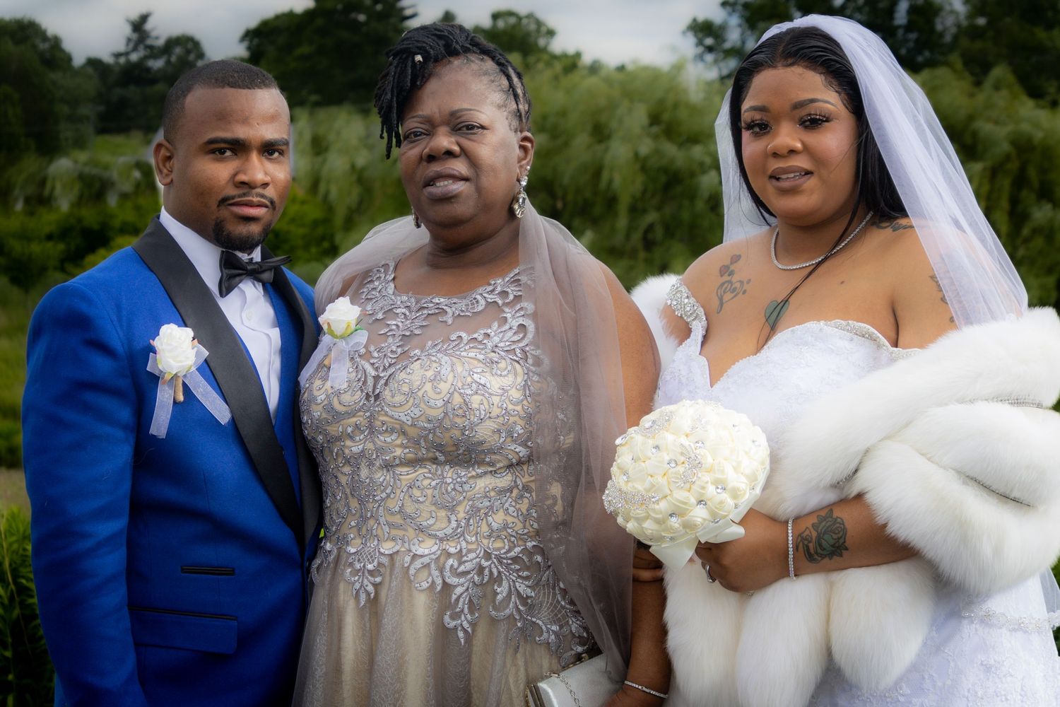 Wedding party members pose together outdoors in elegant blue and silver attire with white floral bouquets.