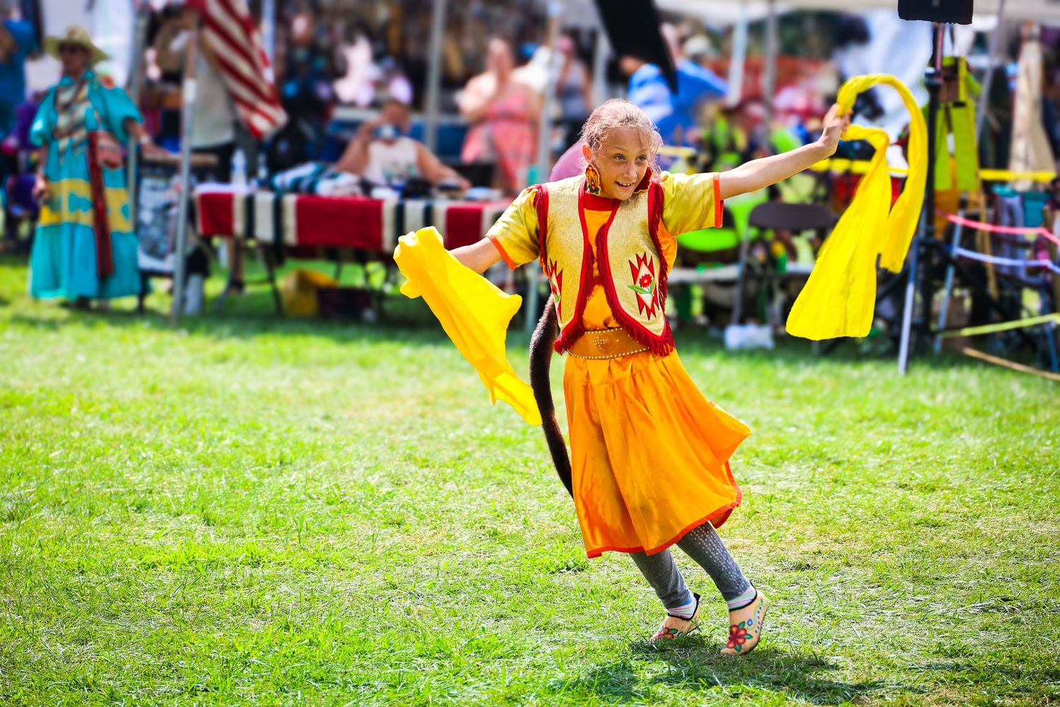 A person in a bright orange dress twirls gracefully on a grassy field during an outdoor event.