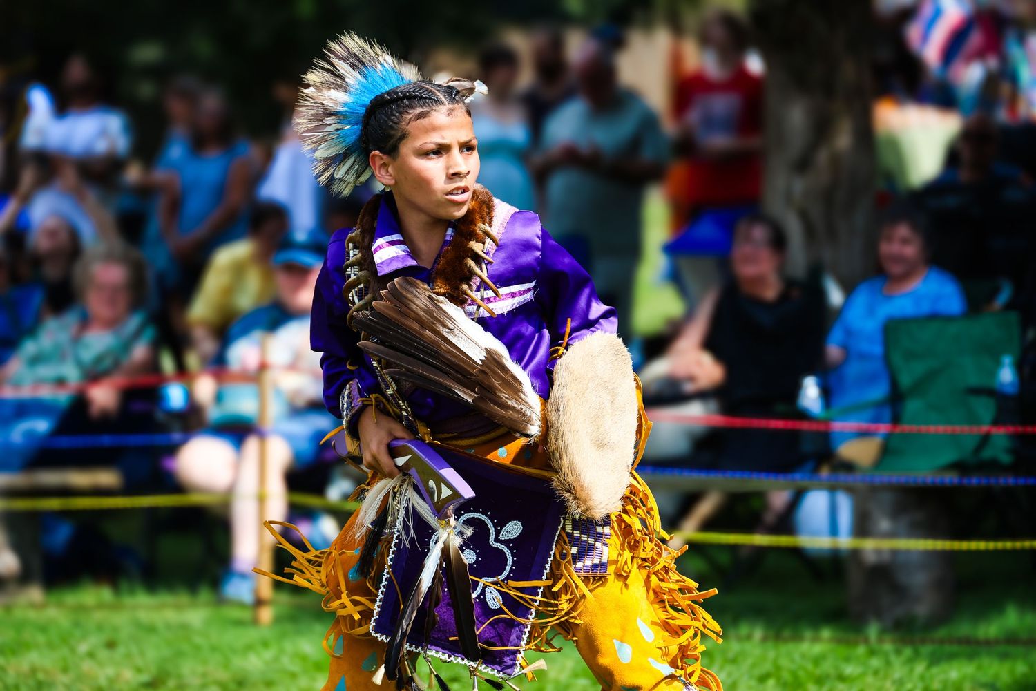 Cheerleaders in purple uniforms perform with yellow pom poms during an outdoor sporting event.