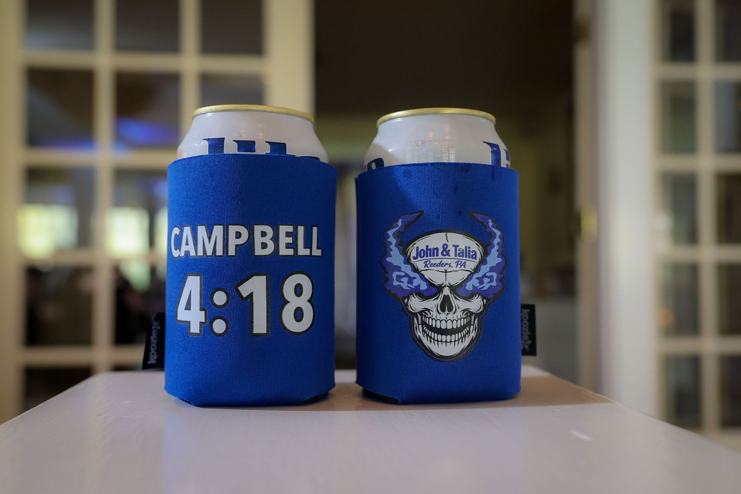 Two blue koozie can coolers, one reading Campbell 4:18 and one featuring a skull design for Jordan & Julia Country Club.