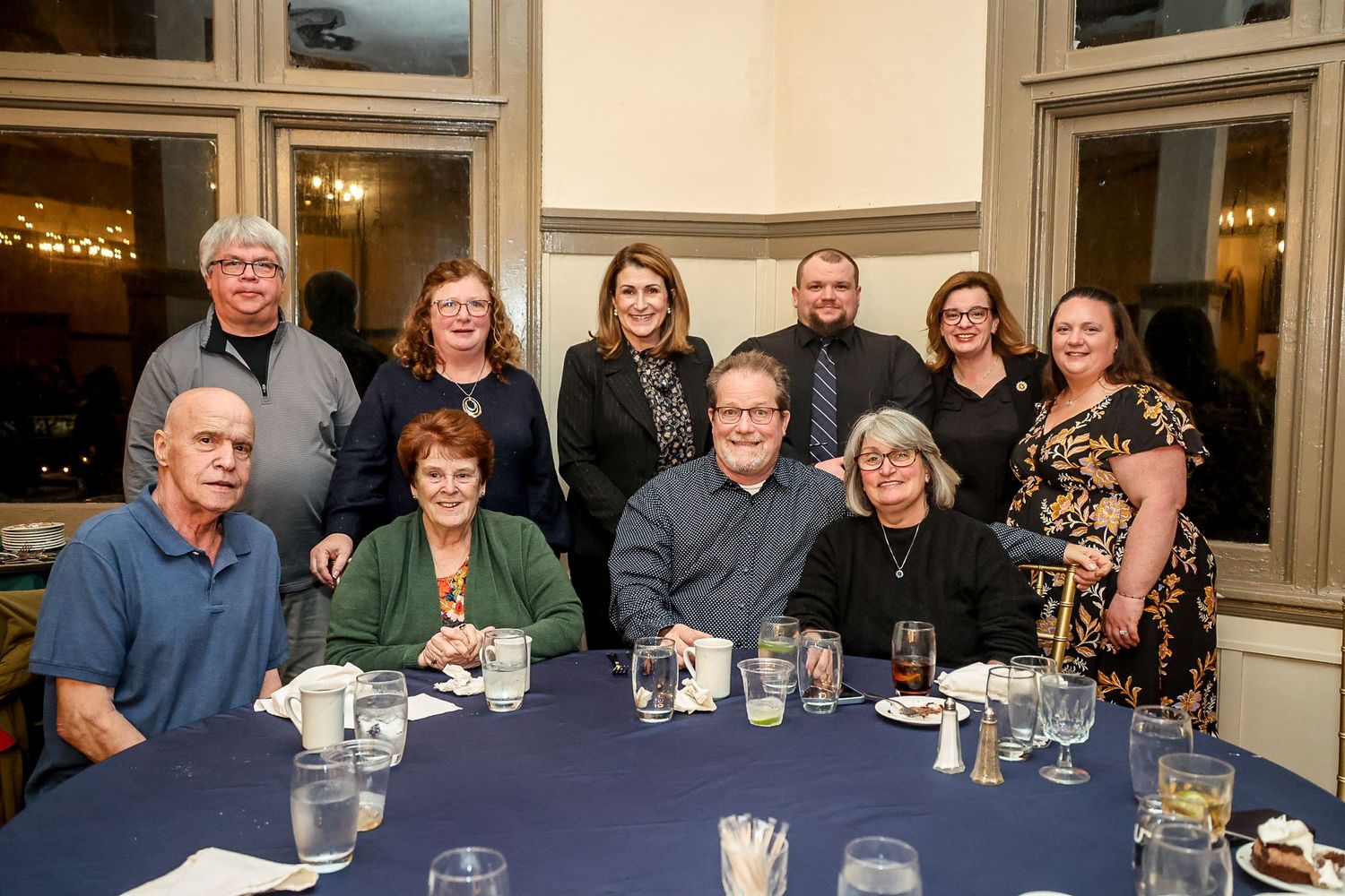 Group of ten people posing for a photo at a formal dinner event, seated and standing around a table with blue tablecloth.