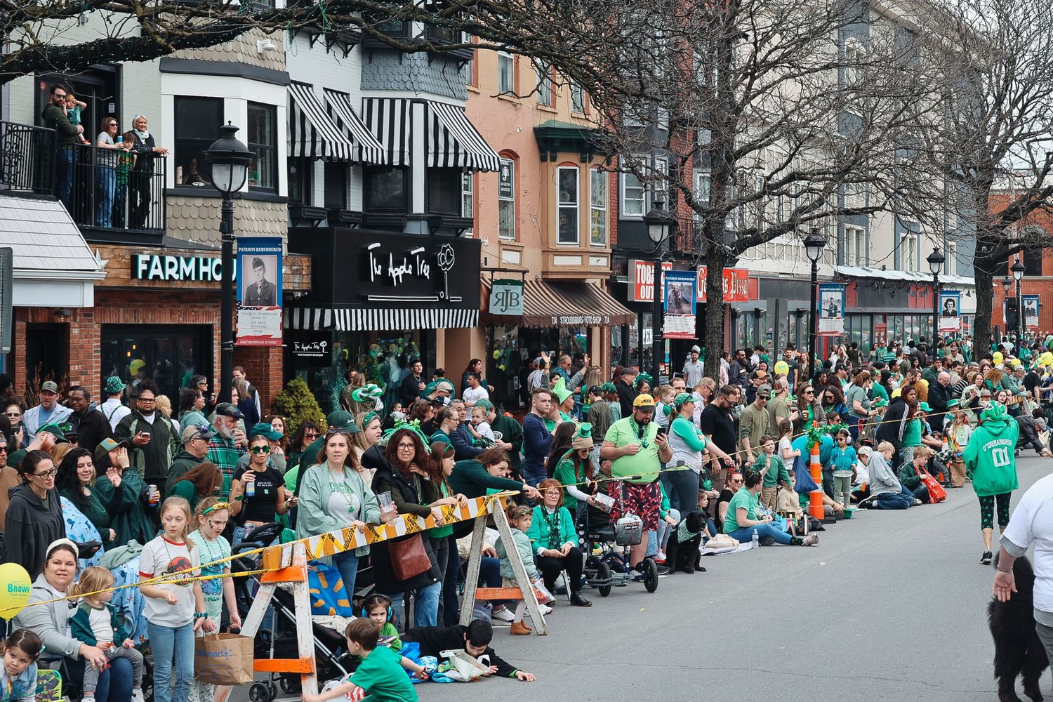 Large crowd dressed in green lines a busy street during a festive St. Patrick's Day parade in a vibrant city.