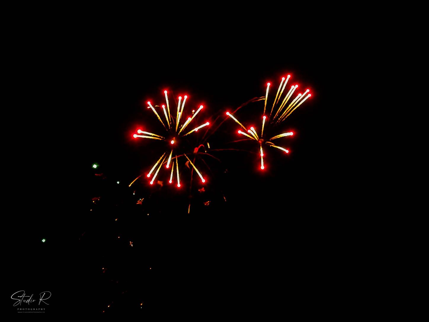 Two vibrant red fireworks burst against a dark night sky, creating dazzling starburst patterns of light.