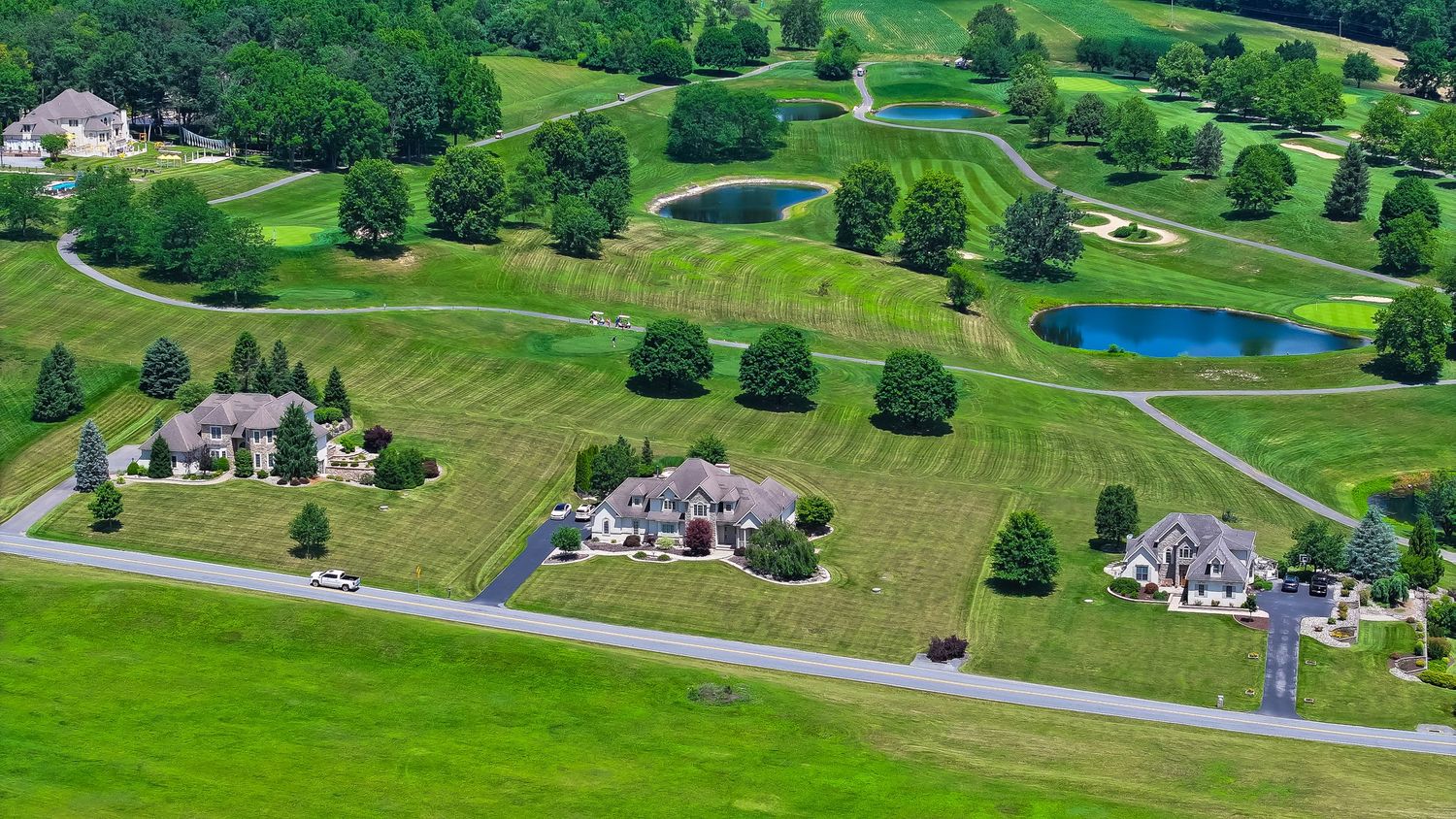 Aerial view of a luxury estate home adjacent to a lush green golf course with ponds and manicured fairways.