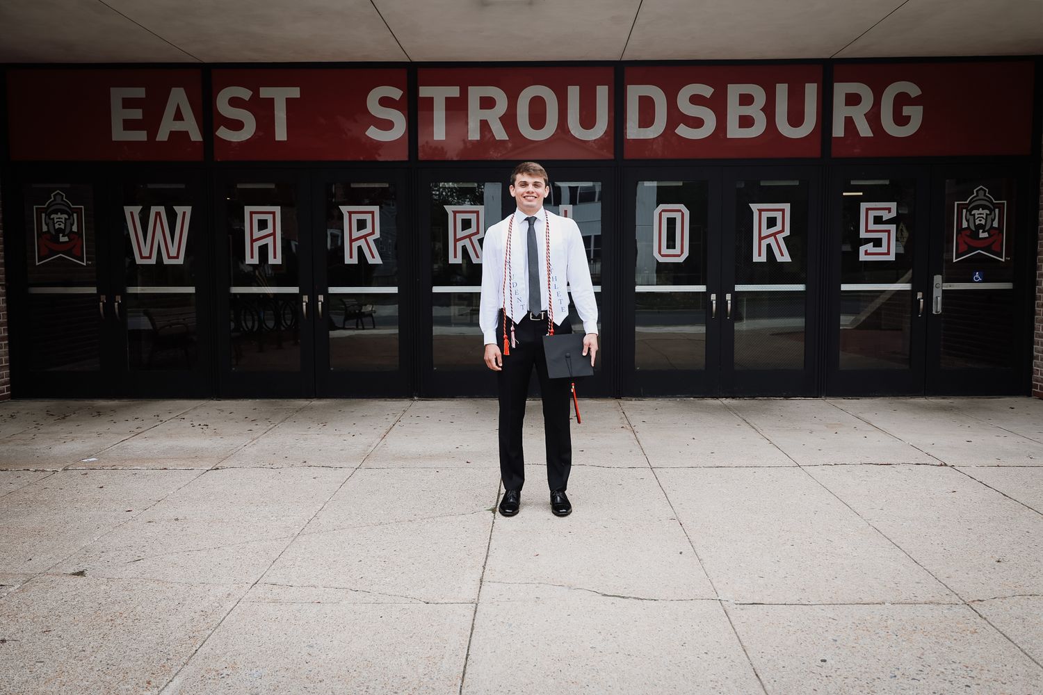 Young man in formal attire standing in front of East Stroudsburg Warriors school entrance doors.