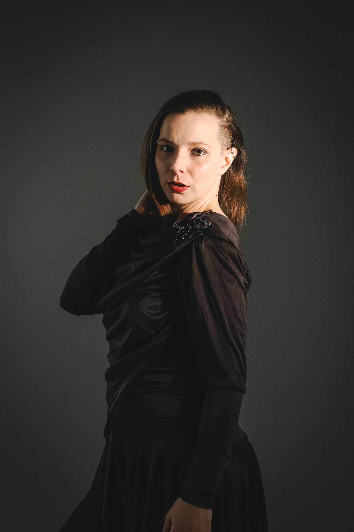 Woman in black dress with red lips poses against dark background in dramatic studio portrait.