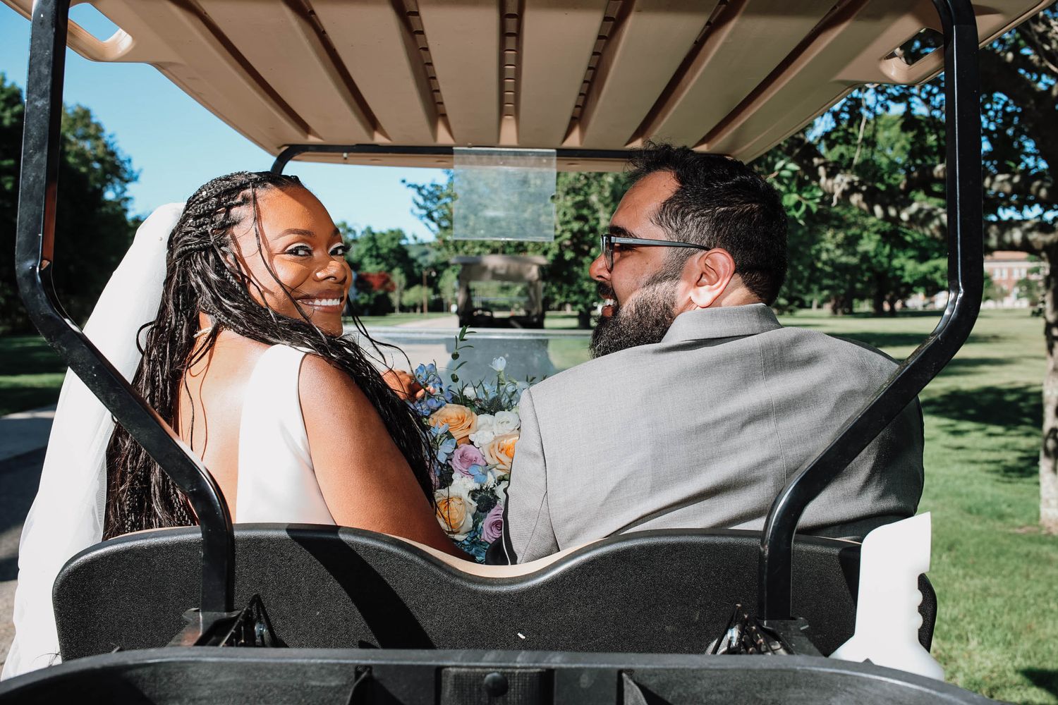 Bride and groom share a joyful moment riding a golf cart outdoors on their wedding day.