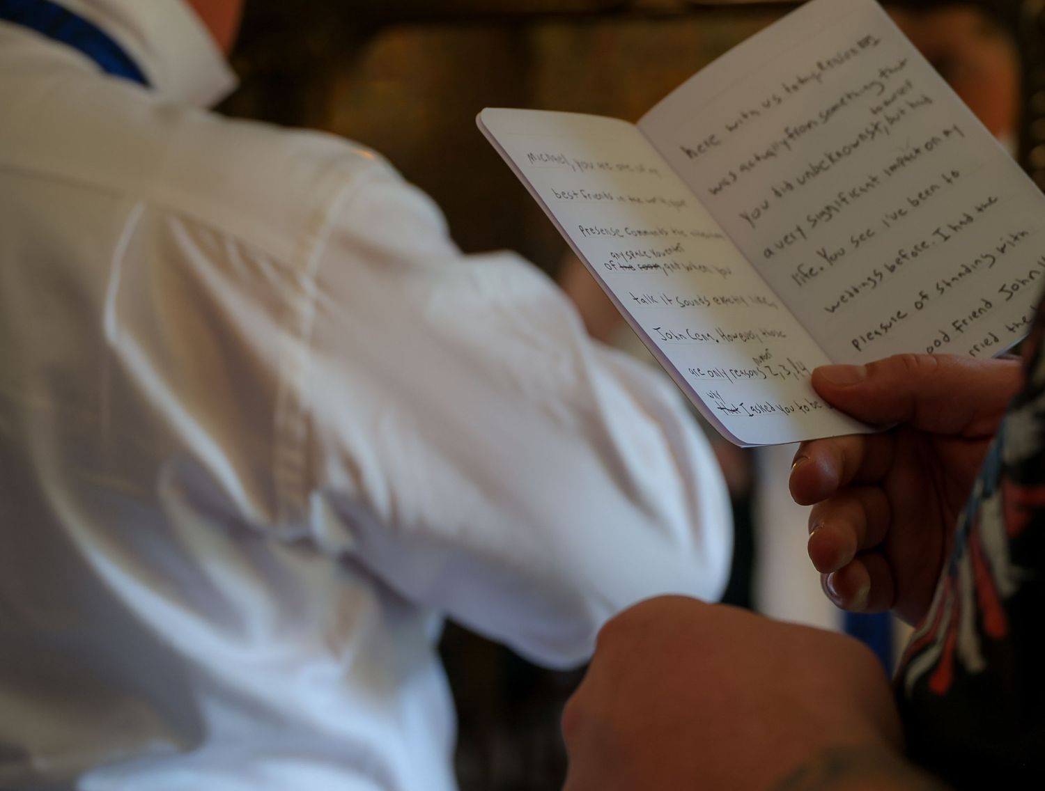Man in white shirt reading handwritten notes in a small notebook at an event or ceremony.