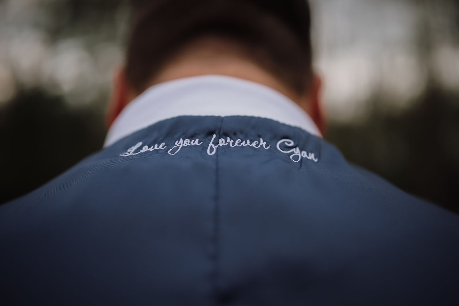 Close-up of a navy suit jacket collar with white embroidered text reading Love you forever Cyan.