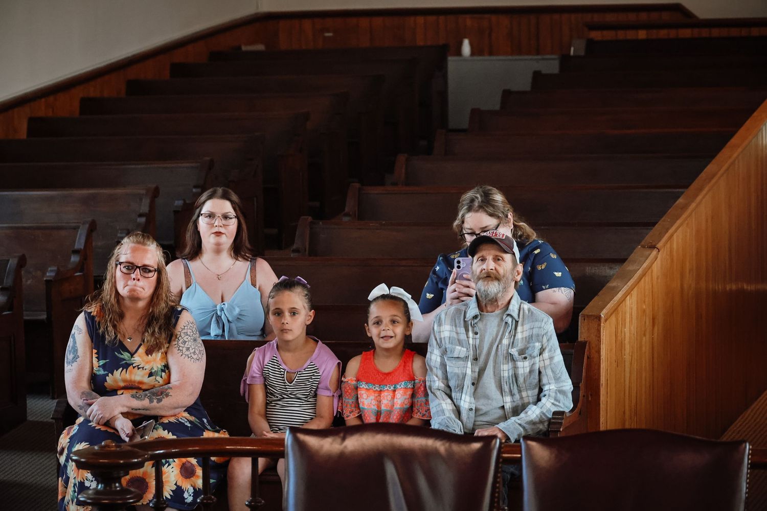 Family group sitting in church pew with wooden stadium seating in background.