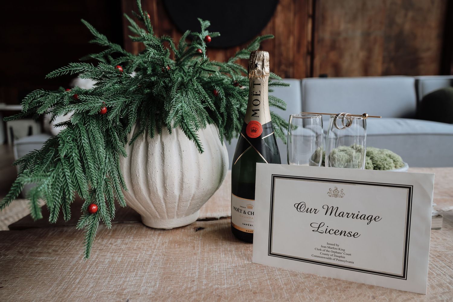 A rustic table setting with a white vase of greenery, wine bottle, and framed sign for bar message service.