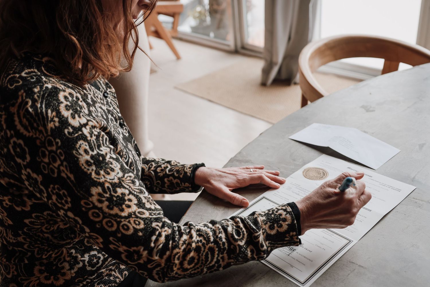 Person reading a book at a wooden table while wearing a floral patterned dress in soft natural lighting.