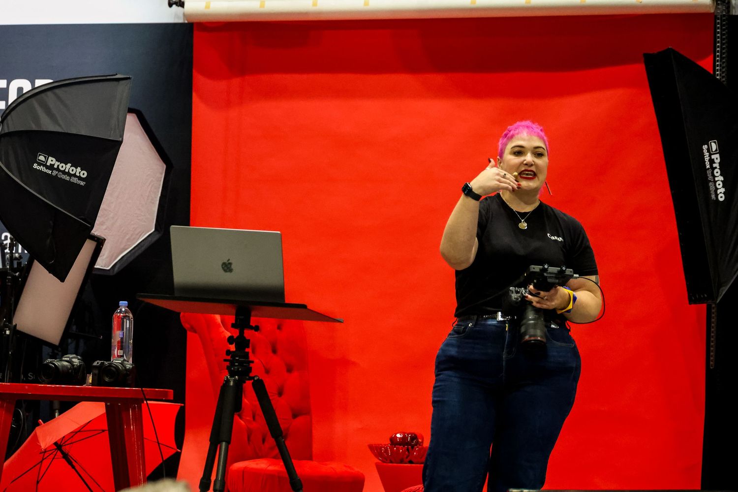 Professional photo studio setup with multiple lights and reflectors against a vibrant red backdrop.