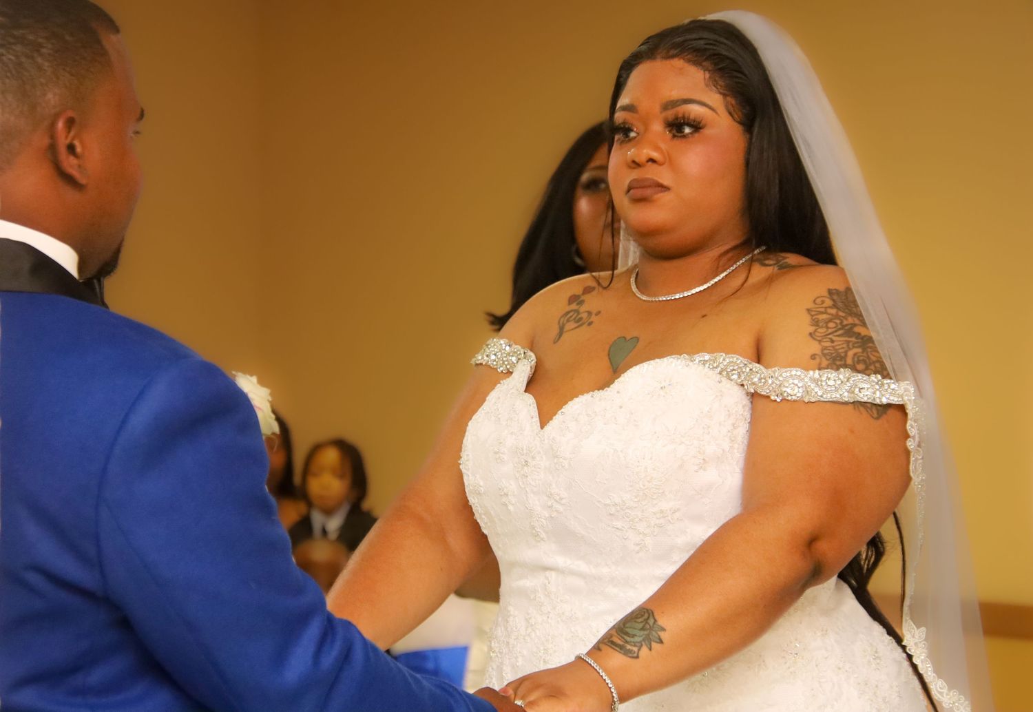 A bride in a white wedding dress dances with her partner in a blue suit at their wedding reception.