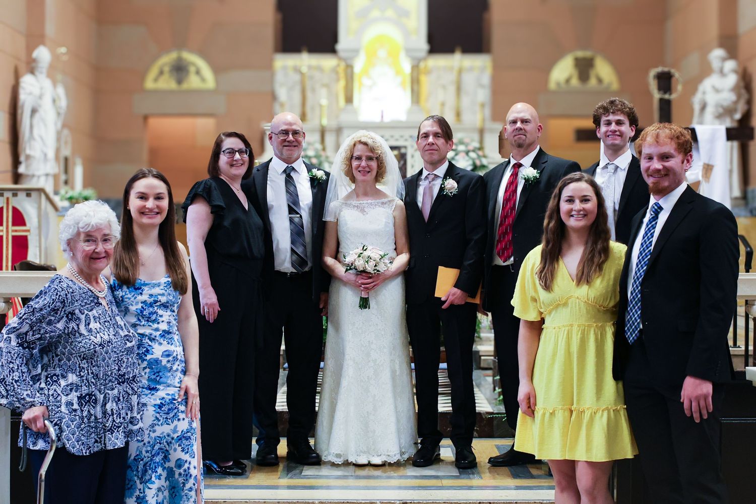A wedding party poses for a formal photo inside a church with ornate statues and arches in the background.