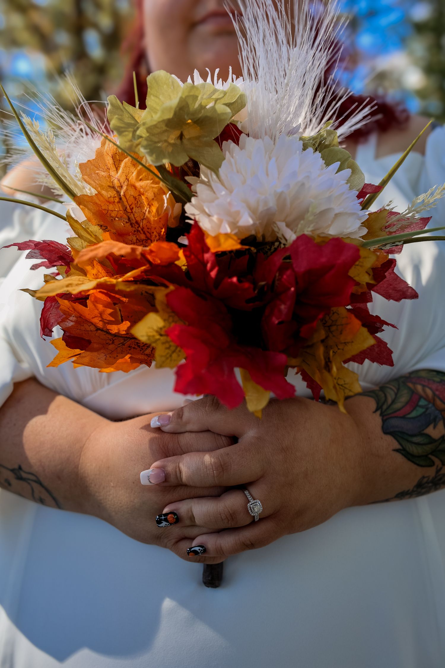 Hands holding a colorful autumn bouquet with red and orange maple leaves mixed with white feathery flowers against a light background.
