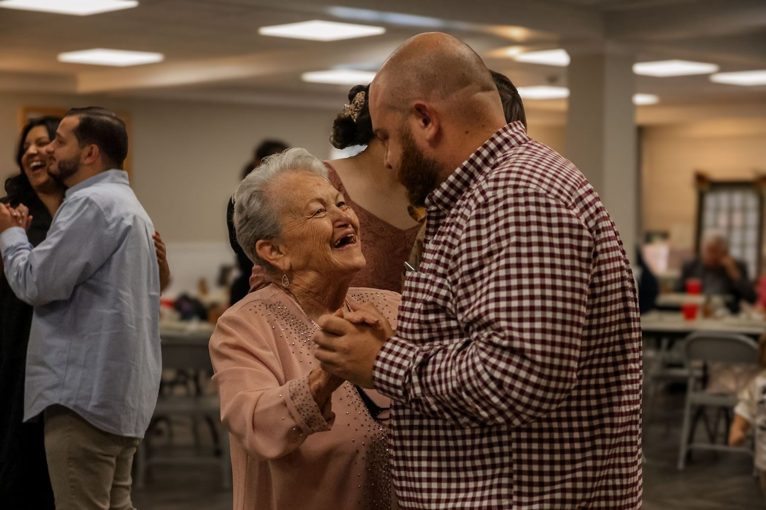 A couple dances together in what appears to be a community center or dance hall.