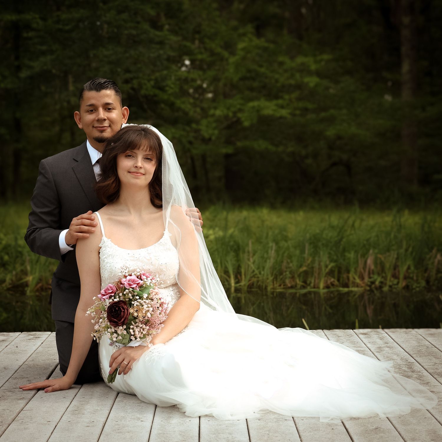 A bride and groom share an intimate moment while sitting on a rustic wooden deck with a natural backdrop.