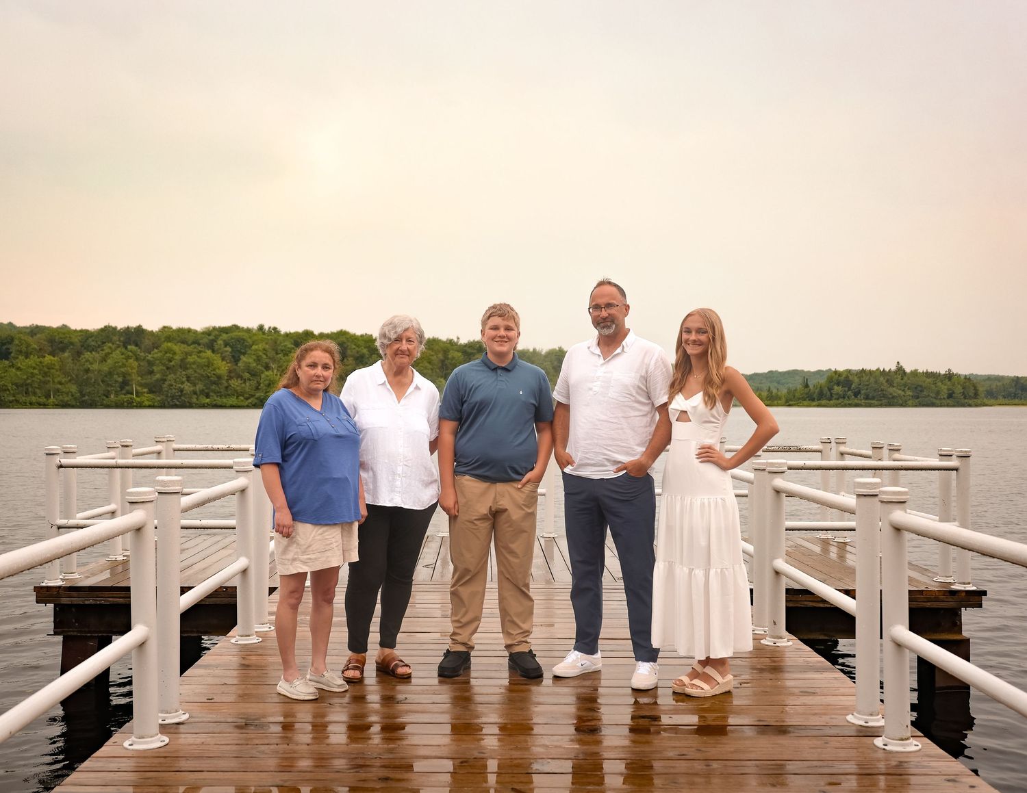 Group of people standing on a wooden pier overlooking a serene lake at sunset.