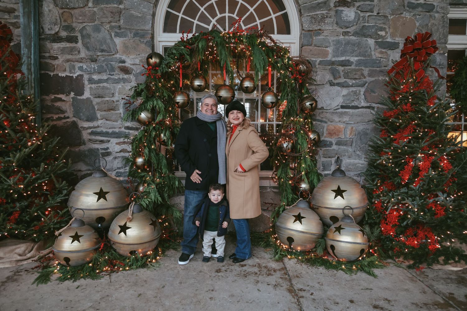 A rustic stone archway decorated with Christmas greenery and red berries creates a festive holiday entrance.