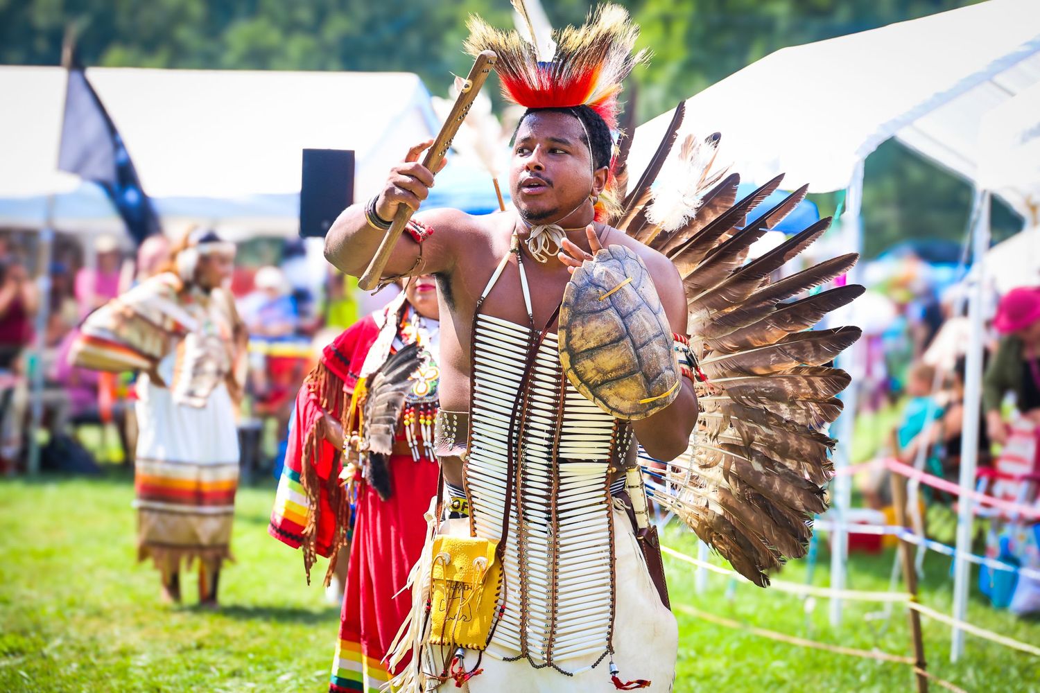 Native American dancers in traditional regalia perform at an outdoor powwow celebration.