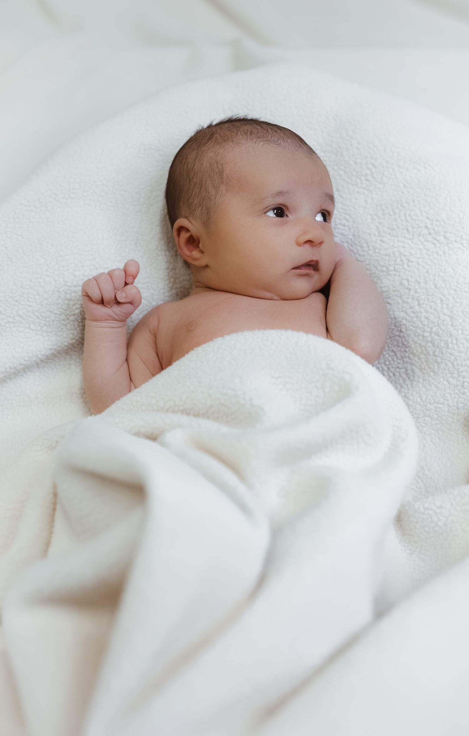 A newborn baby wrapped in soft white blankets rests peacefully against a light background.
