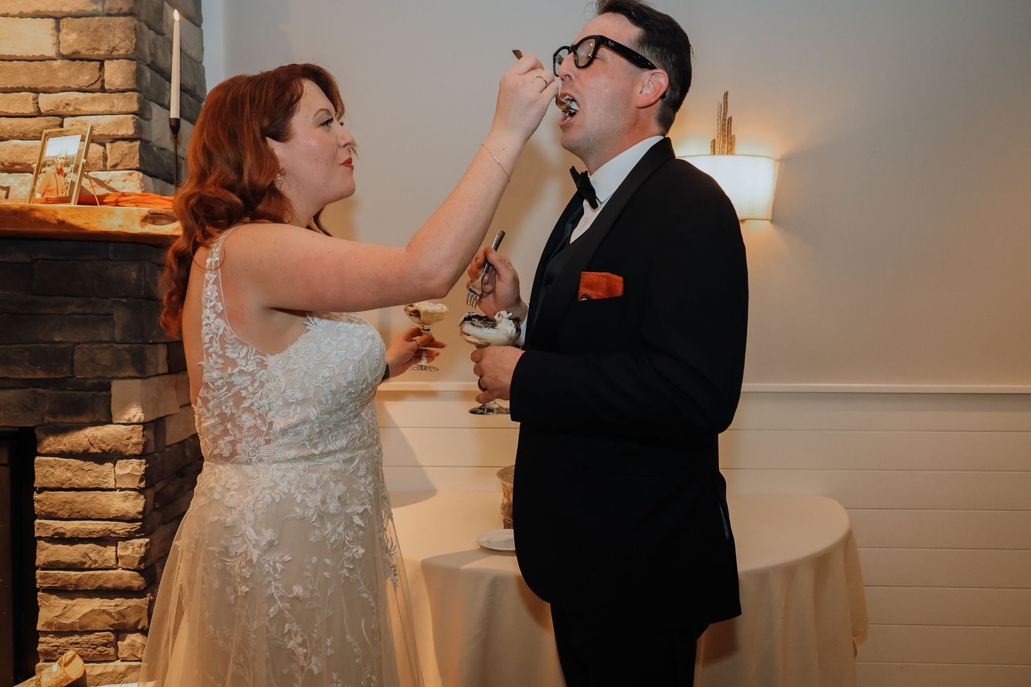 A couple shares a playful moment while feeding each other cake at their wedding reception.